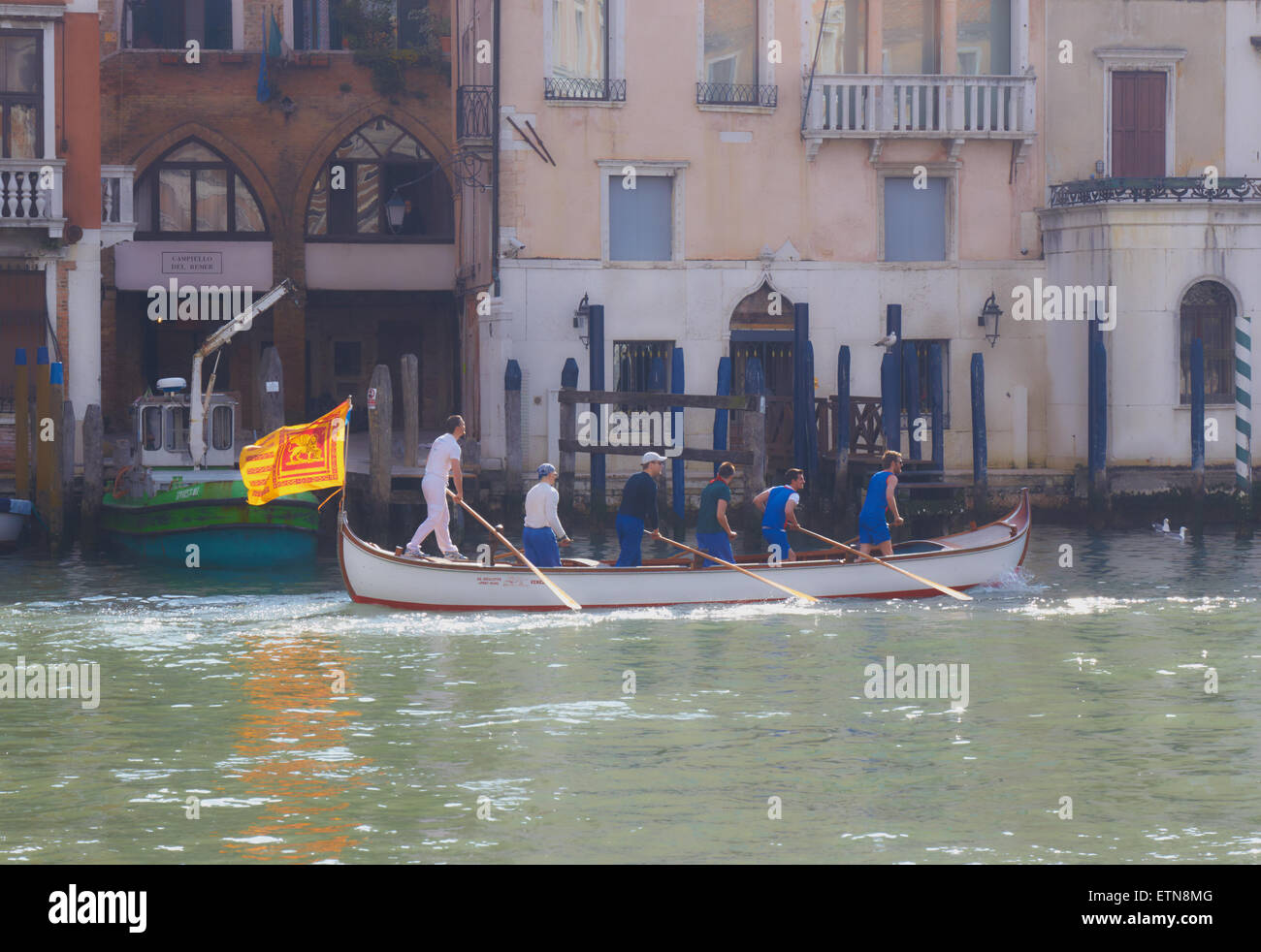 Luce solare nebuloso su una barca remi da sei uomini e battenti la bandiera veneziana di un leone alato che viaggia lungo il Canal Grande Venezia Foto Stock