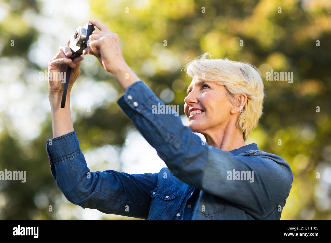 Felice donna matura utilizzando una fotocamera per scattare foto all'aperto presso il parco Foto Stock