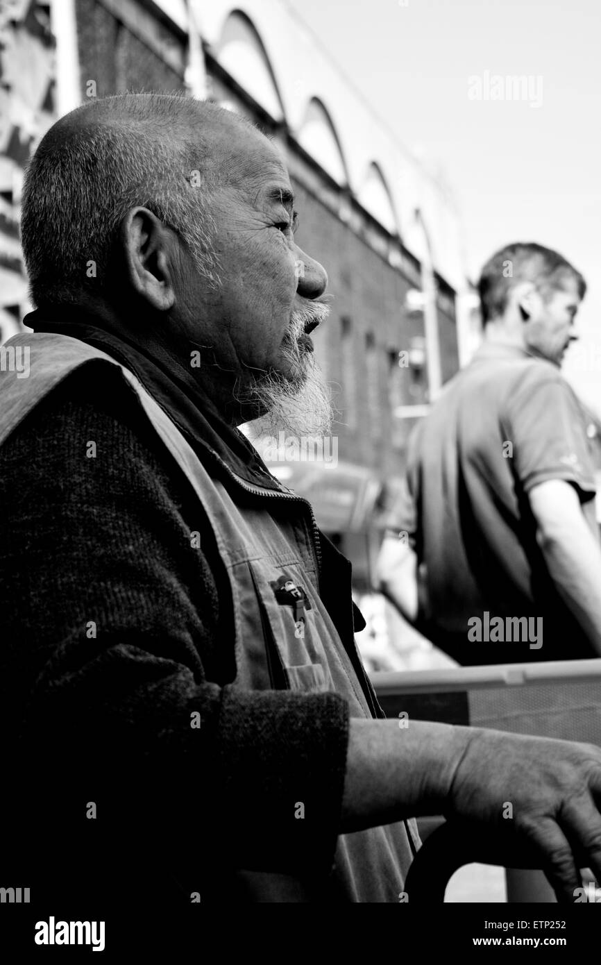 Bianco e nero uomo asiatico cercando di nella distanza da un banco a freshney posto a Grimsby Foto Stock