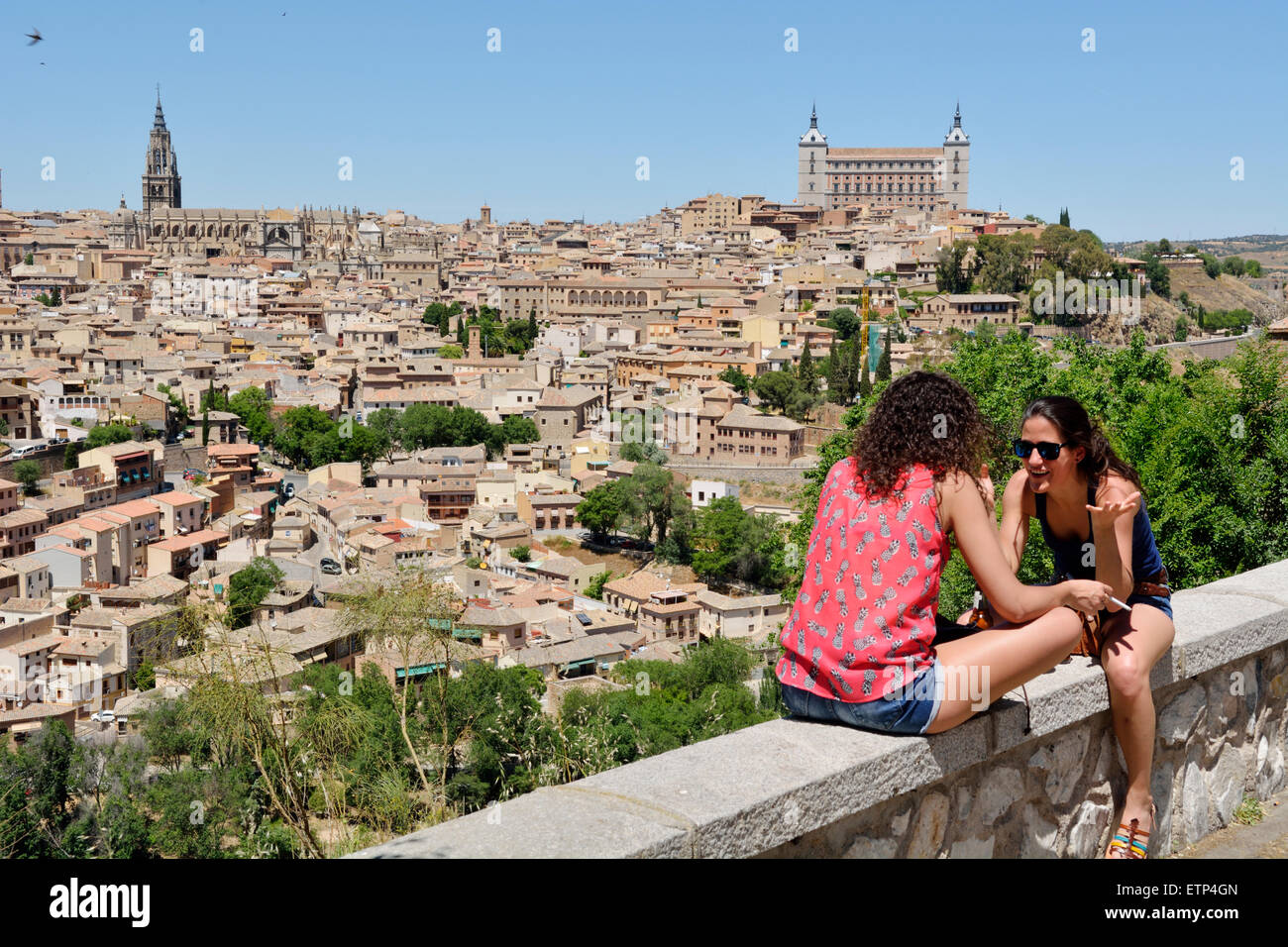 Due donna seduta sulla parete a parlare con la città di Toledo, Spagna in background Foto Stock