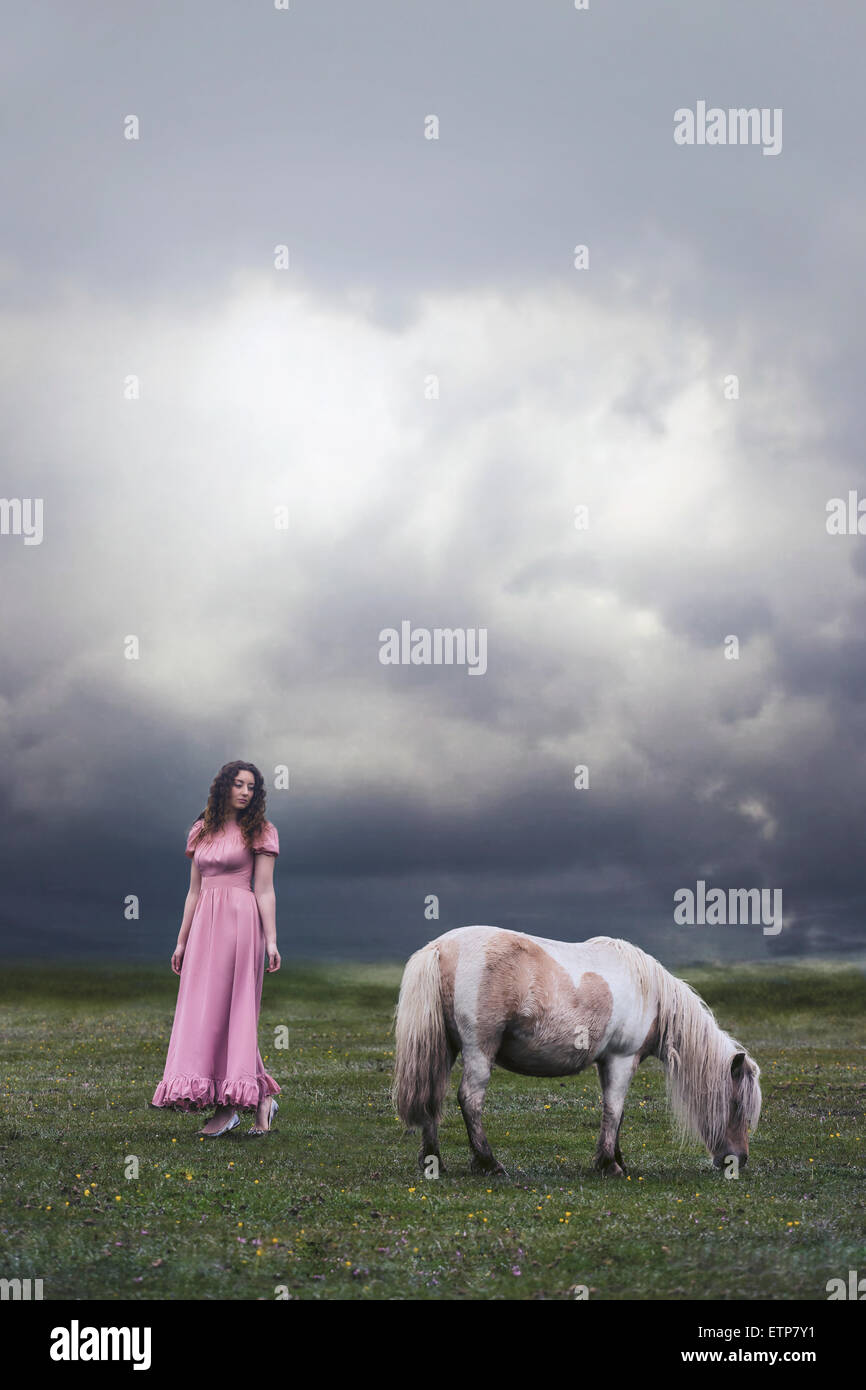 Una ragazza in un abito rosa è in piedi su un paddock con un pony Foto Stock