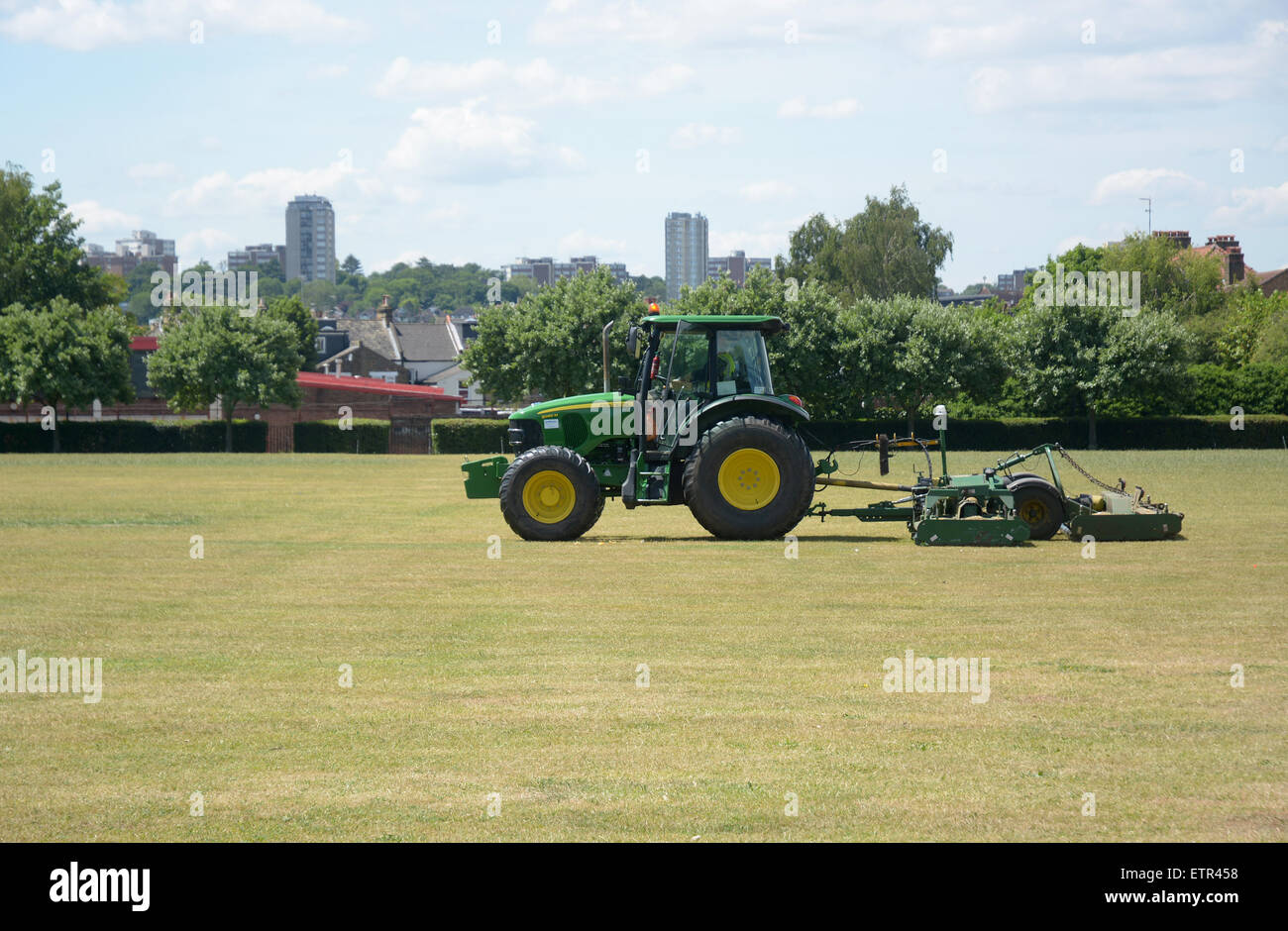 Trattore con attrezzatura di falciatura attaccato il taglio dell'erba in St George's Park Wandsworth SW London Foto Stock