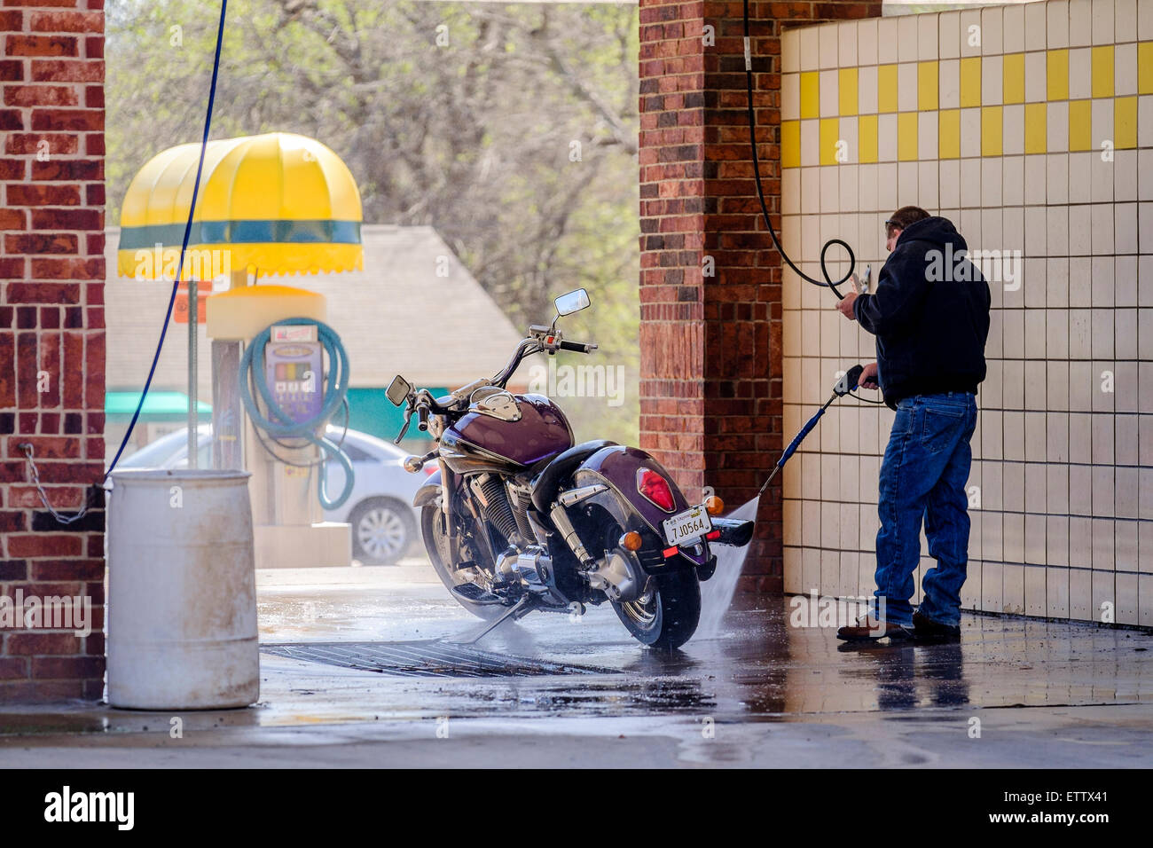 Un uomo lava la sua motocicletta in un gettone per il lavaggio di auto stallo nella città di Oklahoma, Oklahoma, Stati Uniti d'America. Foto Stock