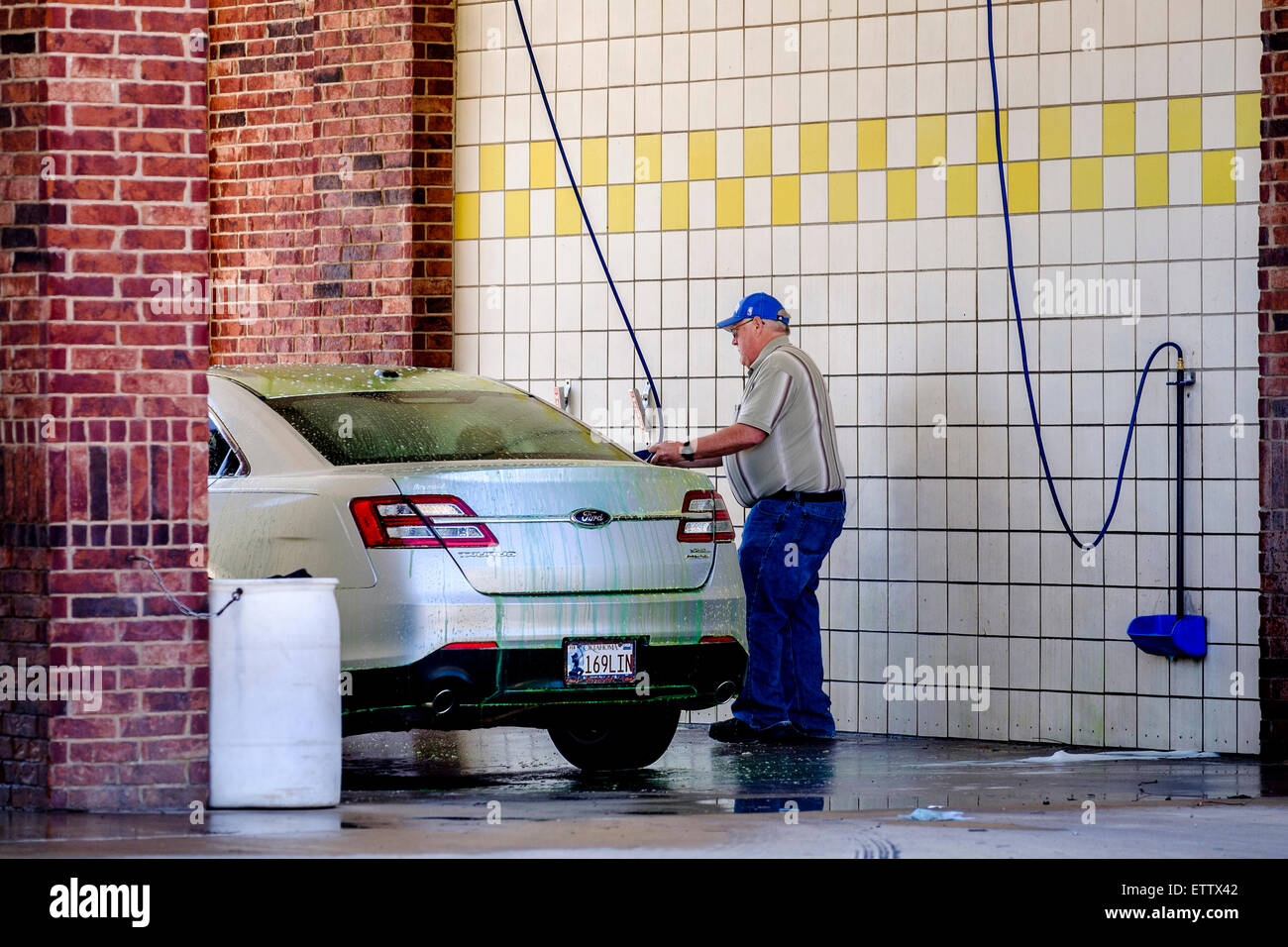 Un anziano uomo caucasico lava il suo argento auto in un gettone per il lavaggio di auto stallo nella città di Oklahoma, Oklahoma, Stati Uniti d'America. Foto Stock