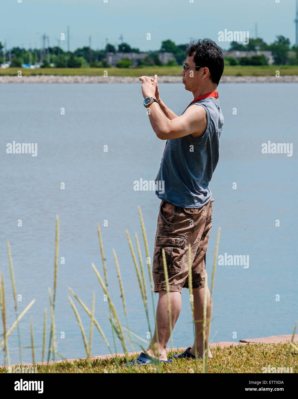 Cinquant'anni di vecchio uomo asiatico scatta foto con il suo telefono cellulare al Lago Hefner nella città di Oklahoma, Oklahoma, Stati Uniti d'America. Foto Stock