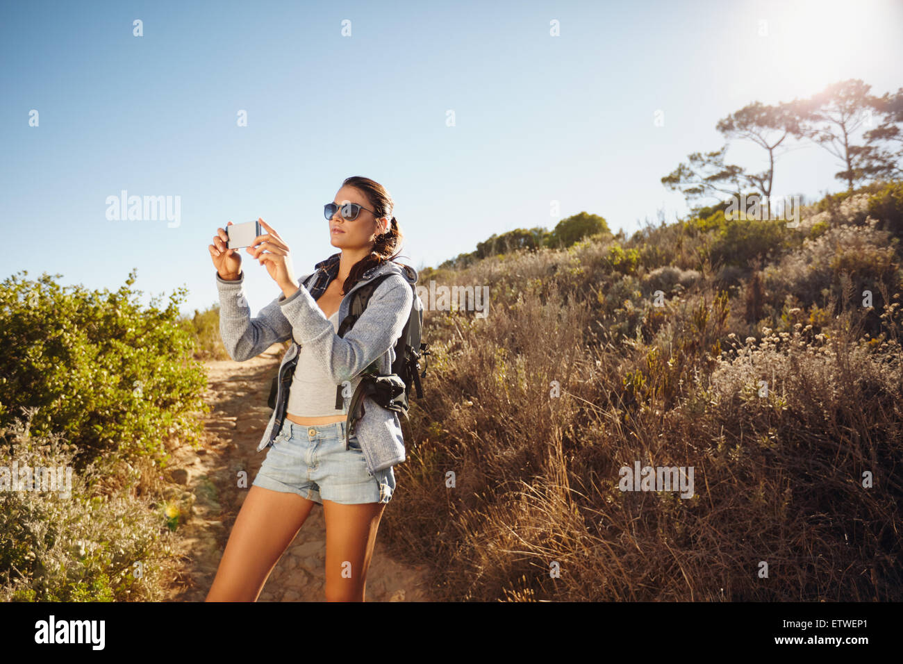 Immagine della giovane donna che parla di fotografie con il suo telefono cellulare durante le escursioni. Femmina caucasica trekking su un giorno d'estate. Foto Stock