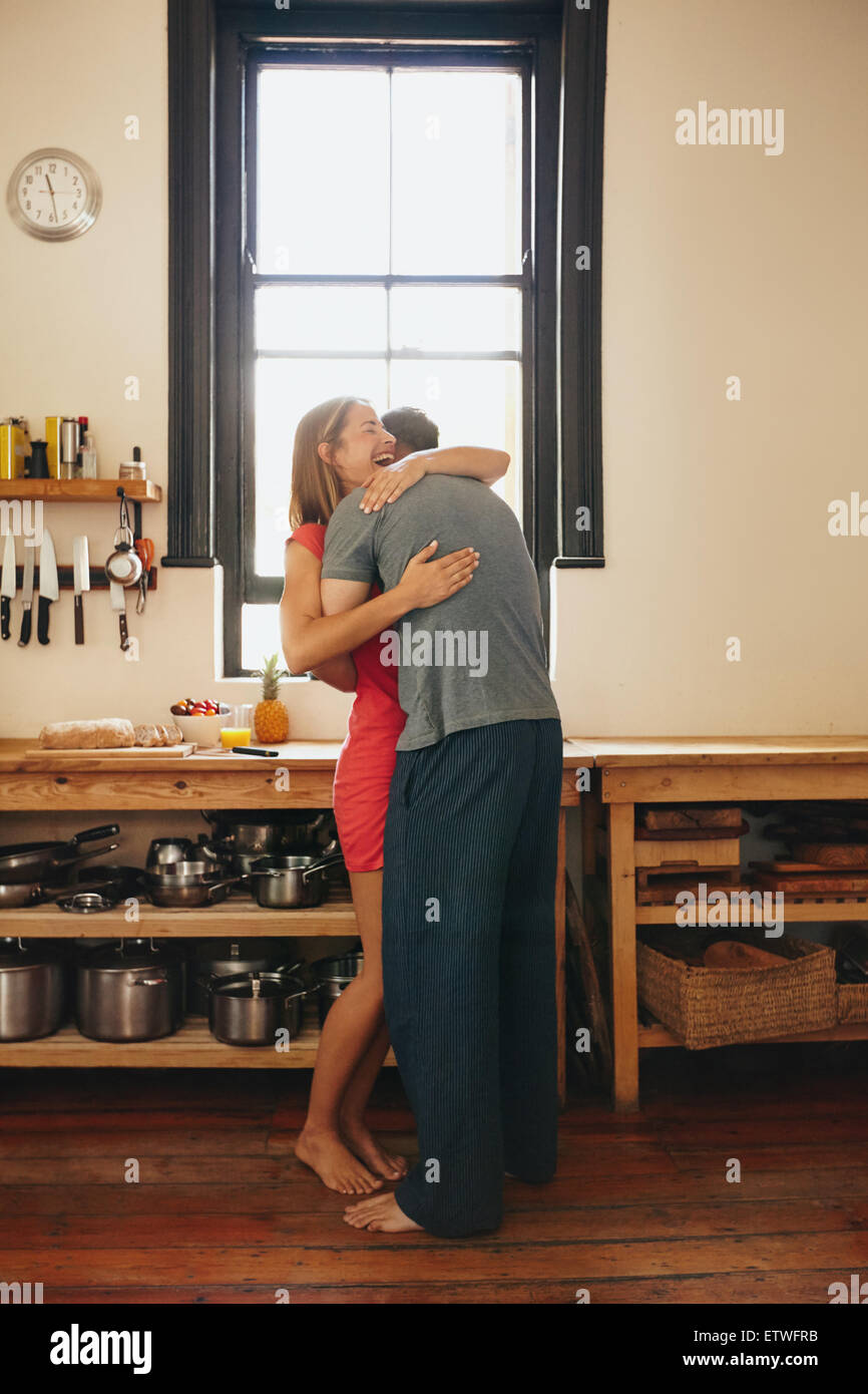 Felice giovane donna essendo abbracciato con il suo fidanzato in cucina. Allegro coppia giovane che abbraccia ogni altra in mattinata a casa. Foto Stock