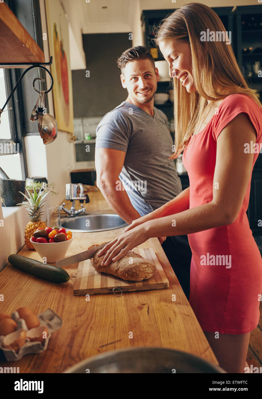 Coppia caucasica insieme in cucina in mattina. Focus sul giovane donna pane di taglio, mentre il marito in attesa. Preparin Foto Stock