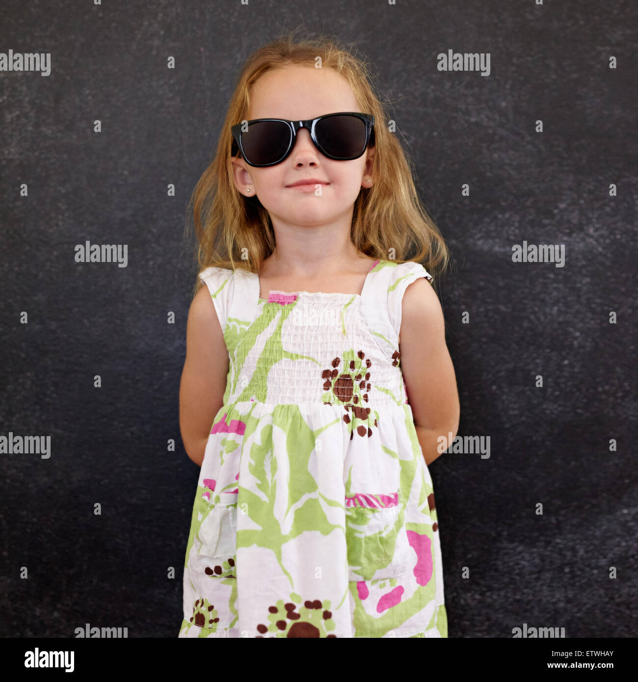 Ritratto di bella bambina indossa occhiali da sole che pongono in telecamera contro un muro nero. Foto Stock