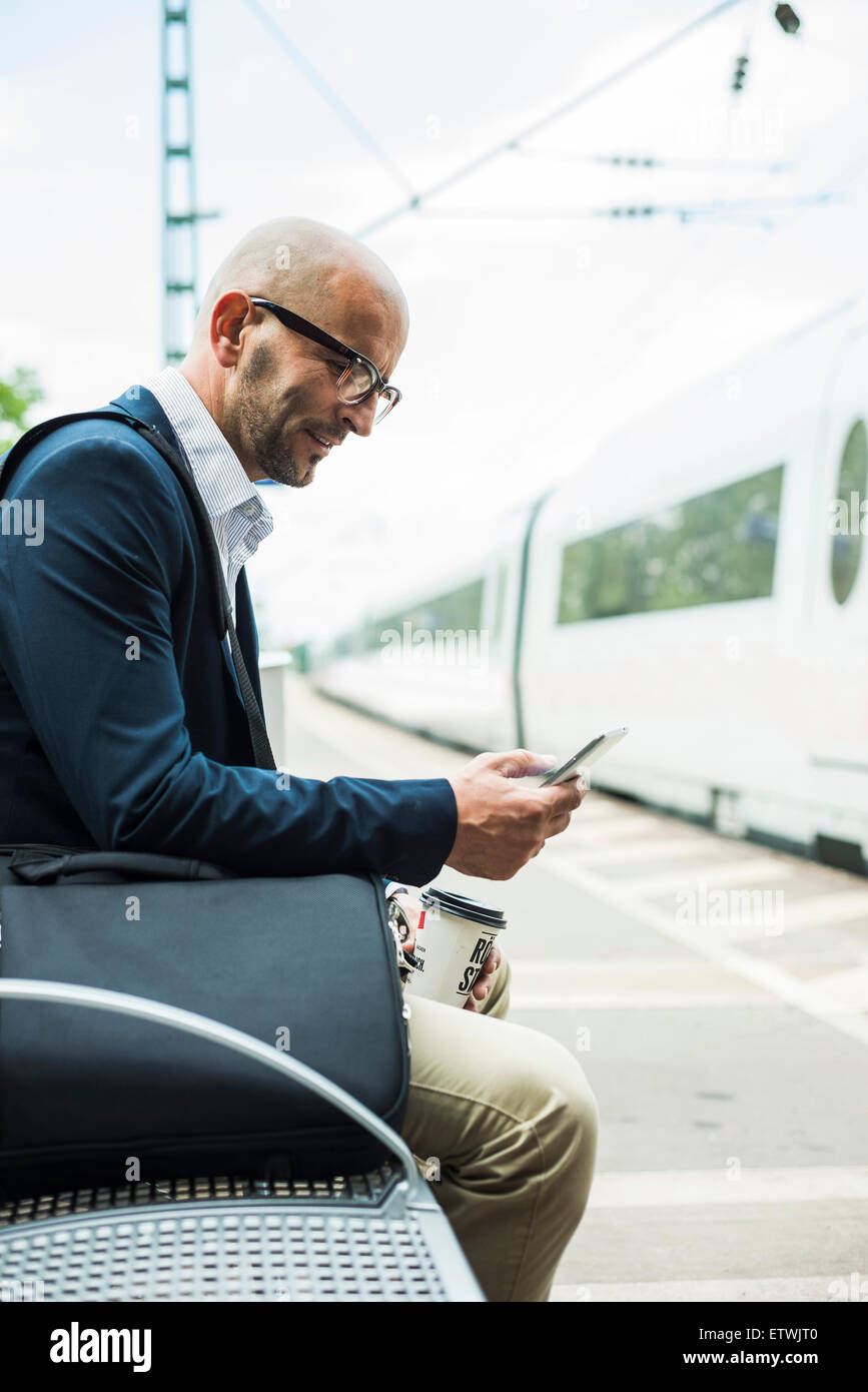 Imprenditore guardando il telefono cellulare sulla piattaforma ferroviaria Foto Stock