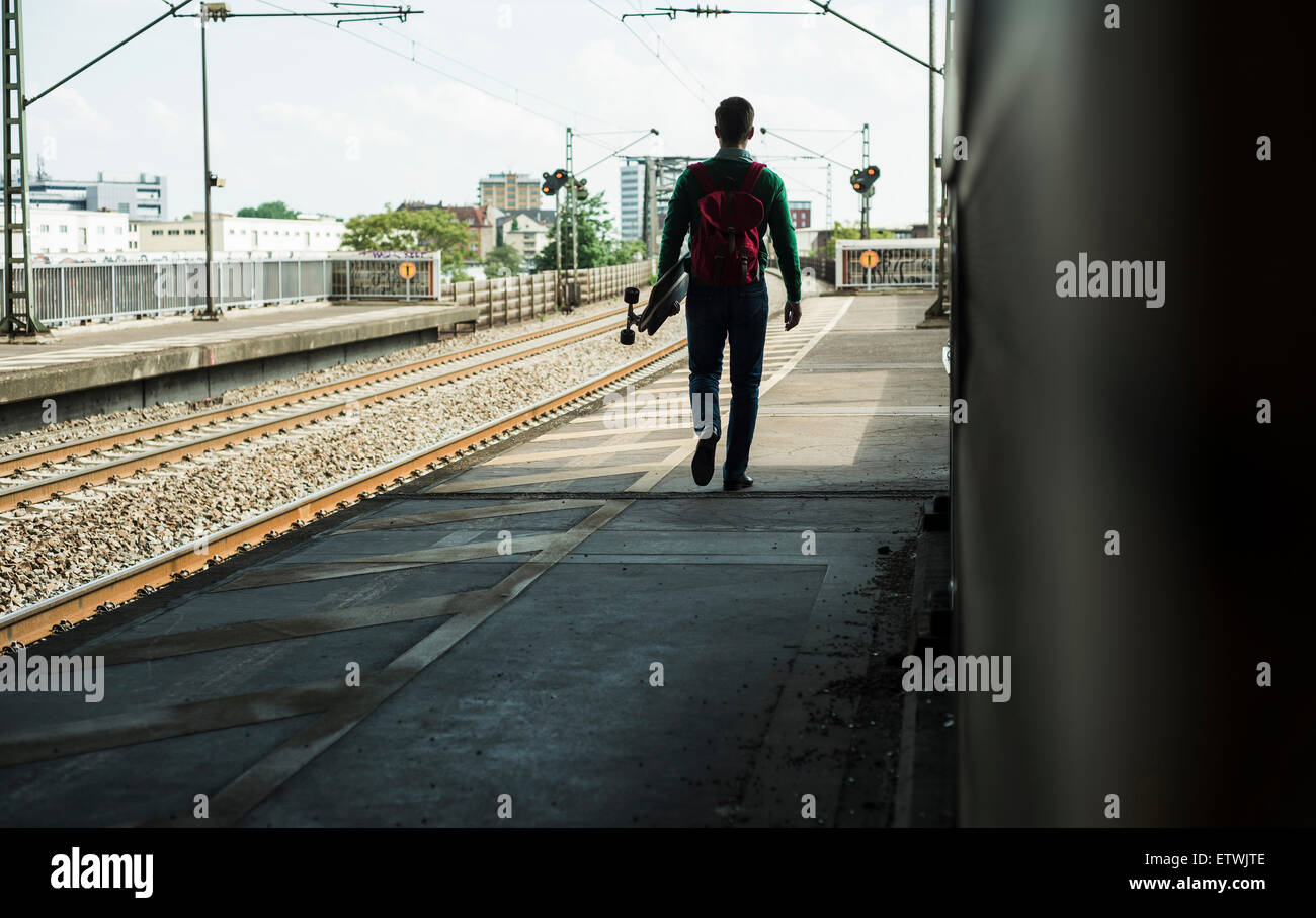 Giovane uomo con lo skateboard a piedi sulla piattaforma ferroviaria Foto Stock