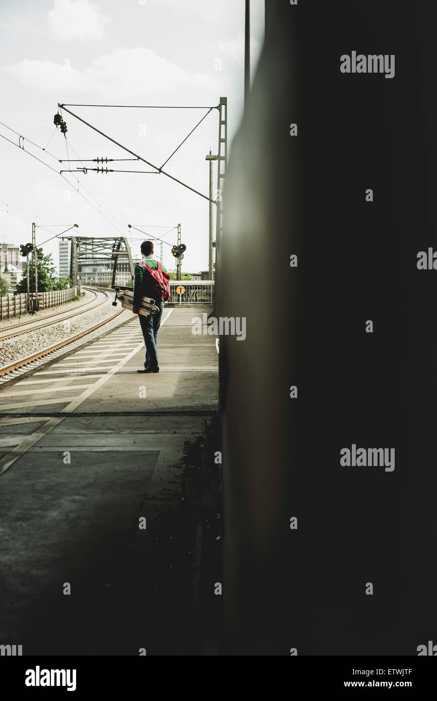 Giovane uomo con lo skateboard in piedi sulla piattaforma ferroviaria Foto Stock