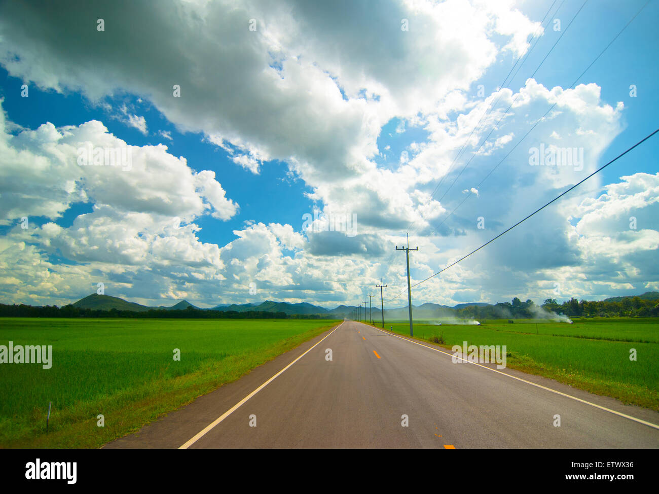 Strada asfaltata attraverso il campo verde e nubi sul cielo blu in estate Foto Stock