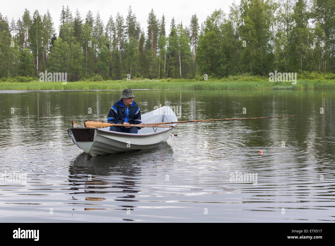 L'uomo, 71 anni, seduti in barca e di pescare con la canna da pesca e la flottazione e la linea, in Boden norrbotten, Svezia Foto Stock