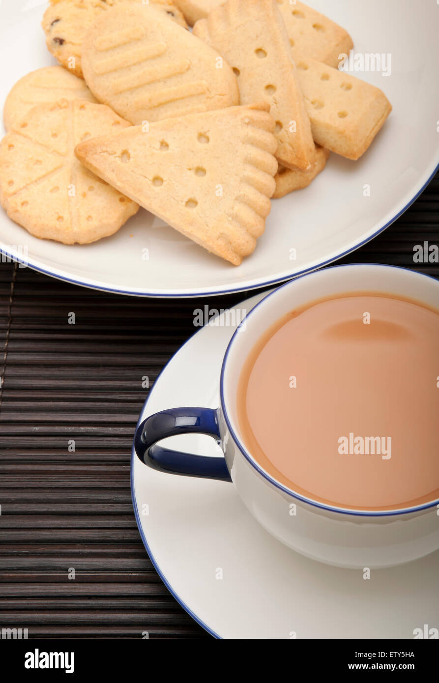 Primo piano di una tazza di tè con il latte su una pentola e un piatto di biscotti frolla dall'alto Foto Stock