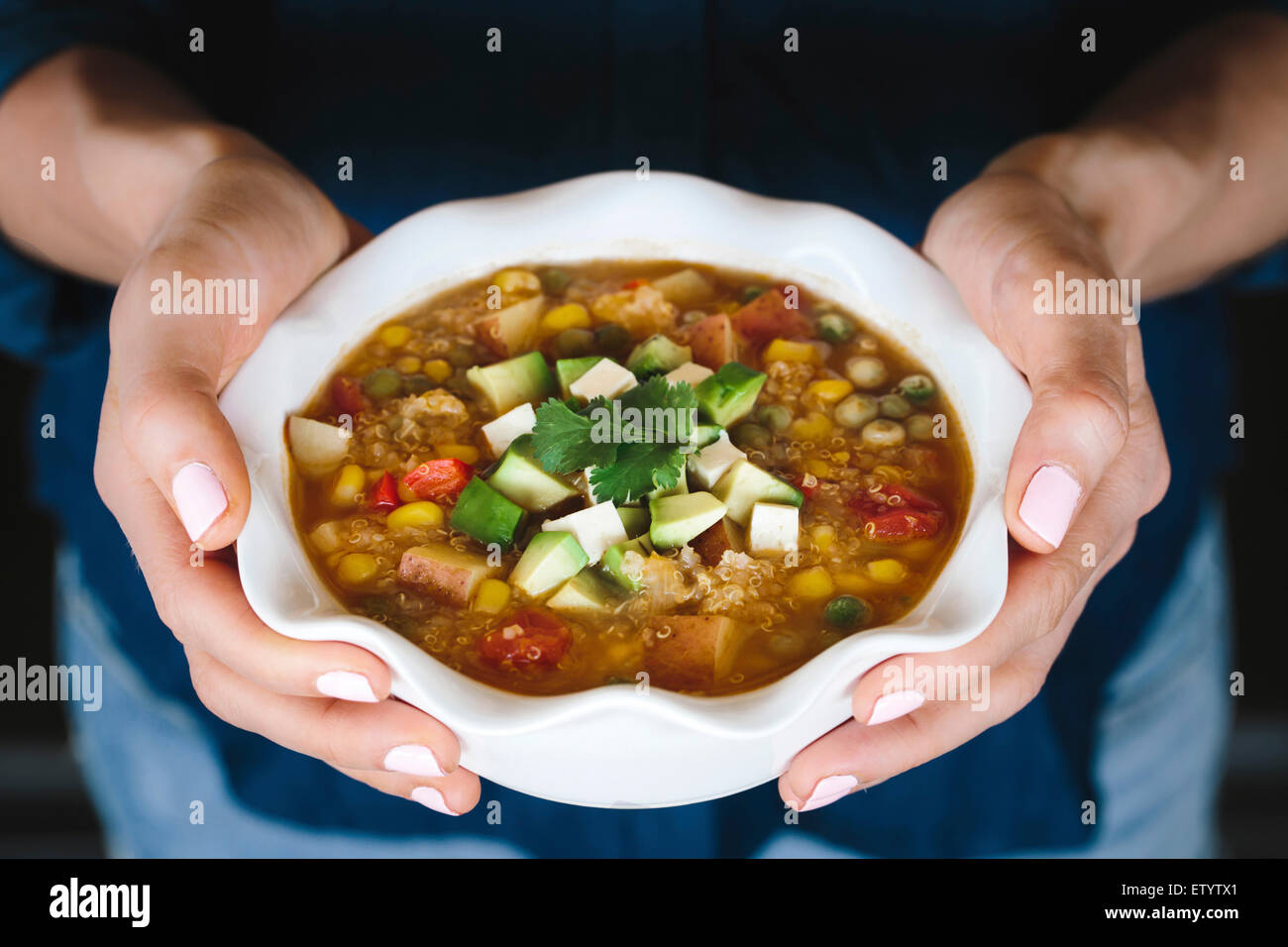 Una tazza di quinoa e estate stufato di verdure farcite con dadolata di avocado, queso blanco e una foglia di coriandolo viene visualizzata in una Foto Stock