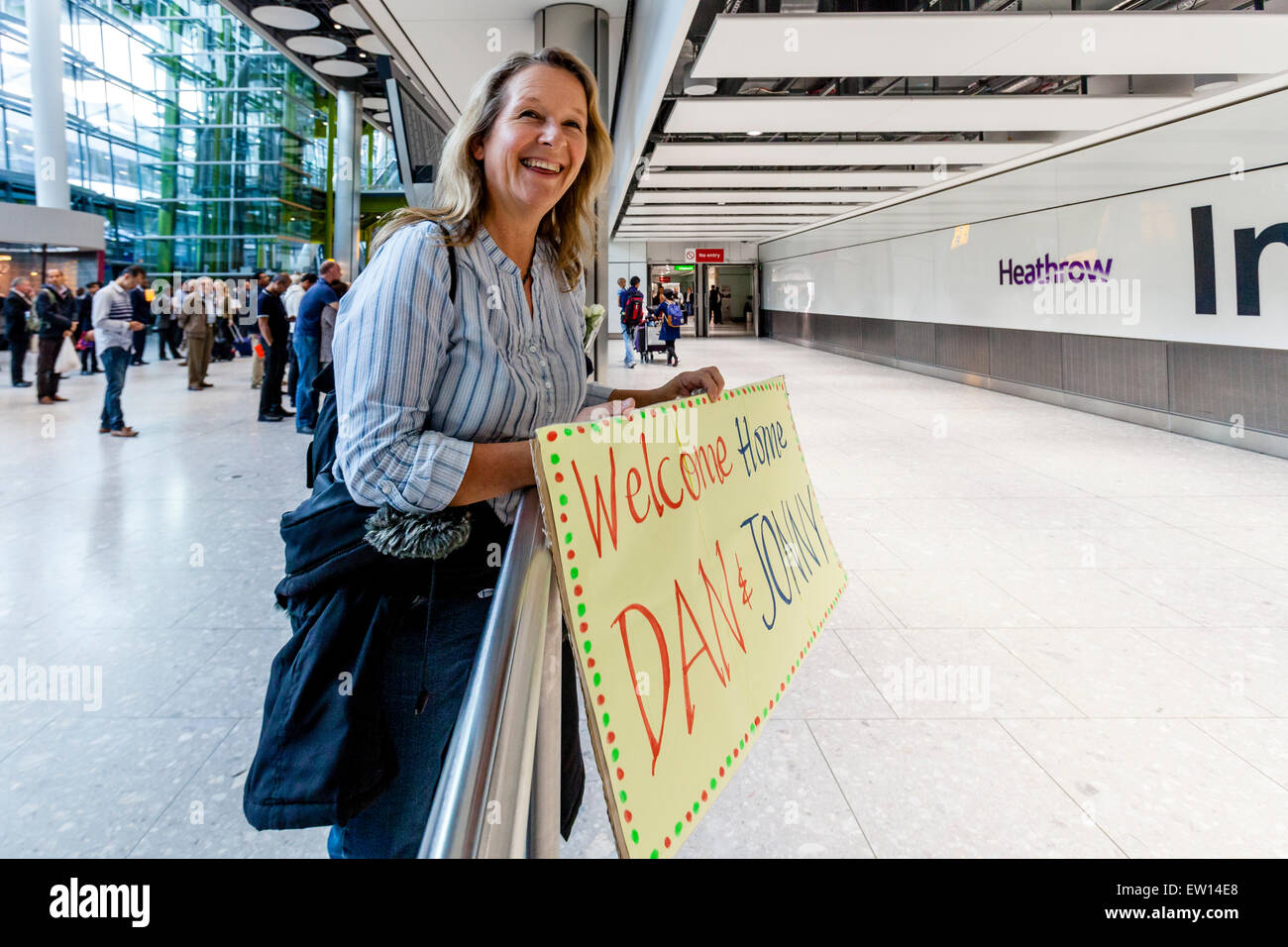 Una mamma sorregge un segno ad accogliere il suo figlio e il suo amico a casa dal viaggio, l'aeroporto di Heathrow a Londra, Inghilterra Foto Stock