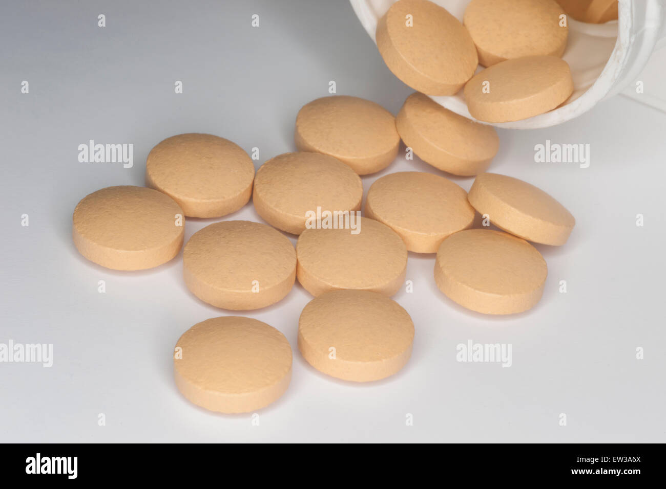 Tablet medications fuoriuscita da una bottiglia di plastica bianca su una superficie bianca. Foto Stock