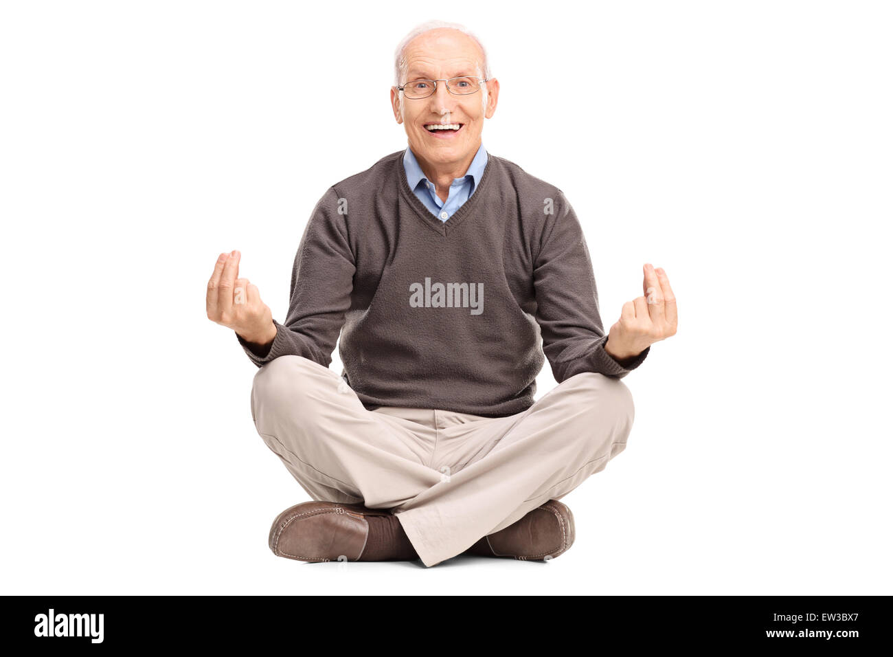 Gioiosa senior gentleman meditando seduto sul pavimento e guardando la telecamera isolata su sfondo bianco Foto Stock