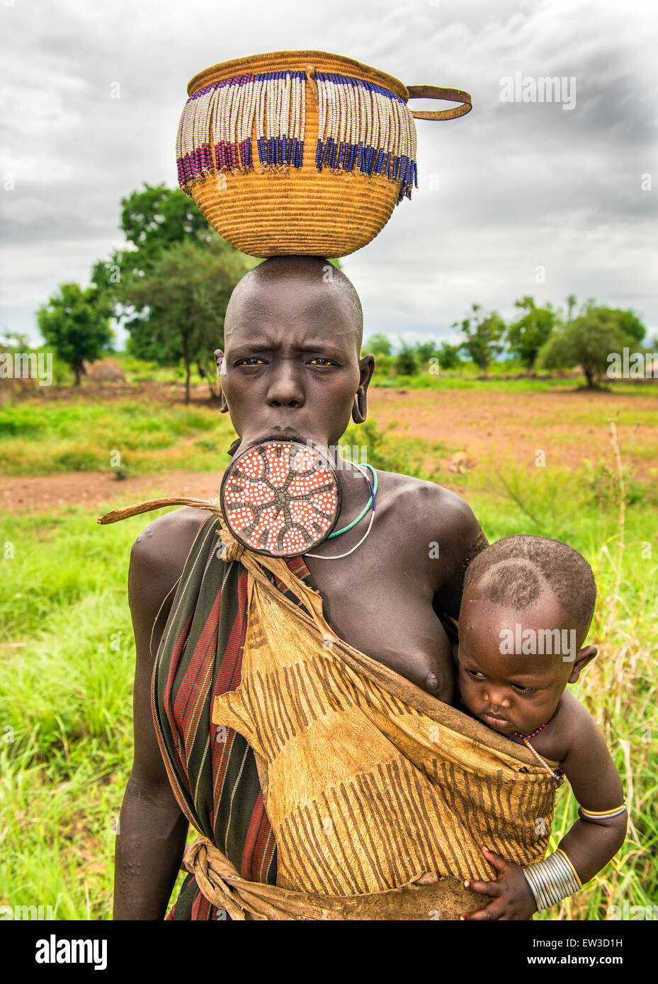 Una donna dalla tribù africana Mursi con labbro grande piastra che porta il suo bambino. Foto Stock