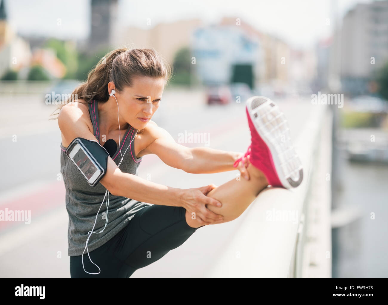 Un atletico donna si allunga prima di andare su un lungo periodo. Lei sta indossando un bracciale sul suo braccio che tiene il suo dispositivo. Su di esso, Foto Stock