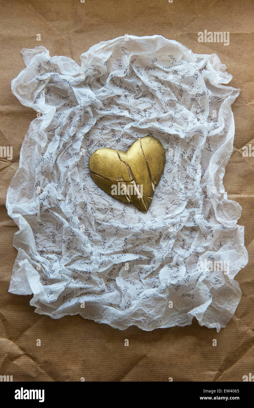 In frantumi, oro dipinto di cuore su carta velina bianca con la scritta la parola amore.carta marrone sfondo Foto Stock