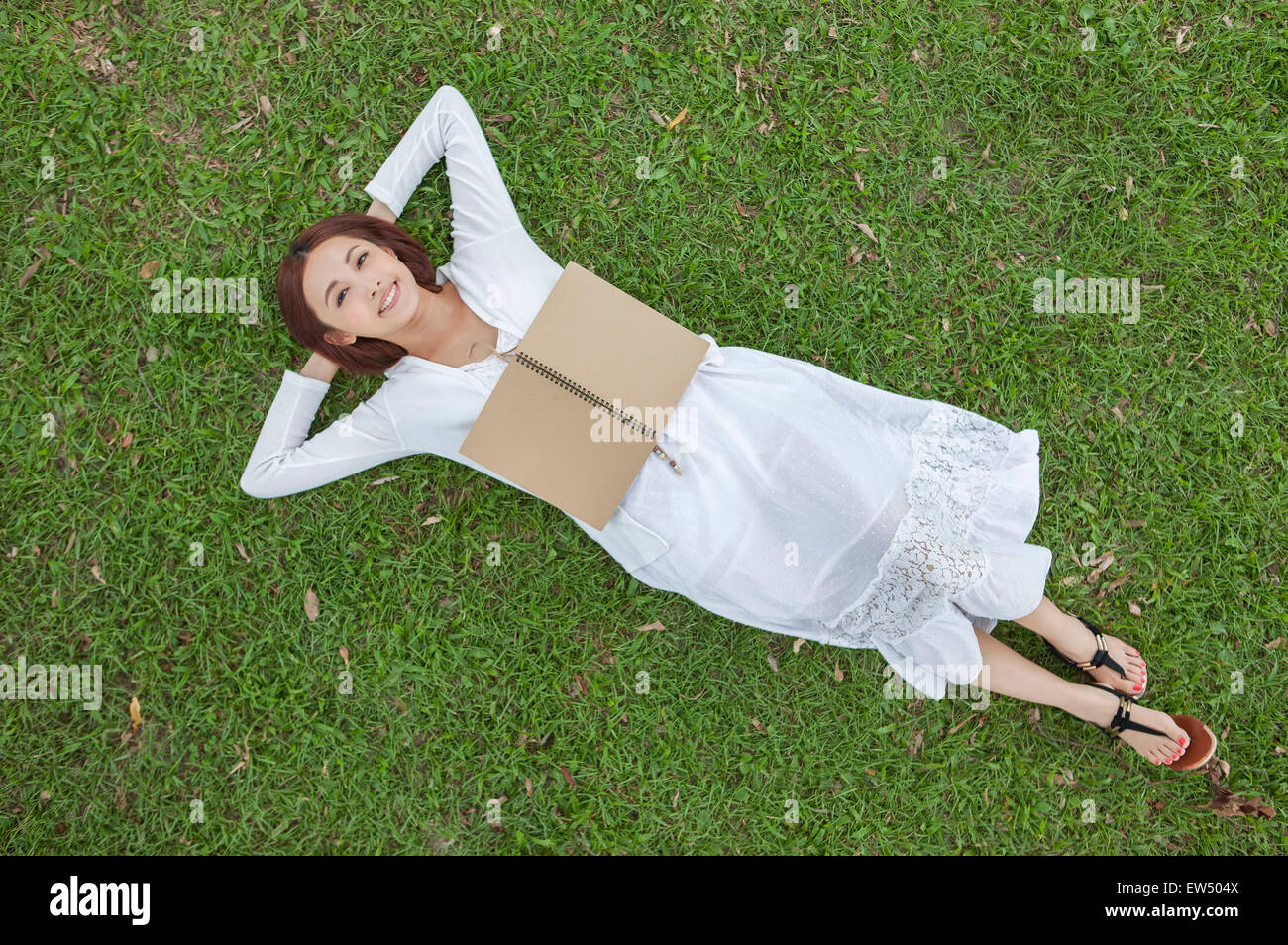 Giovane donna sdraiata sul prato con le mani la testa benind Foto Stock