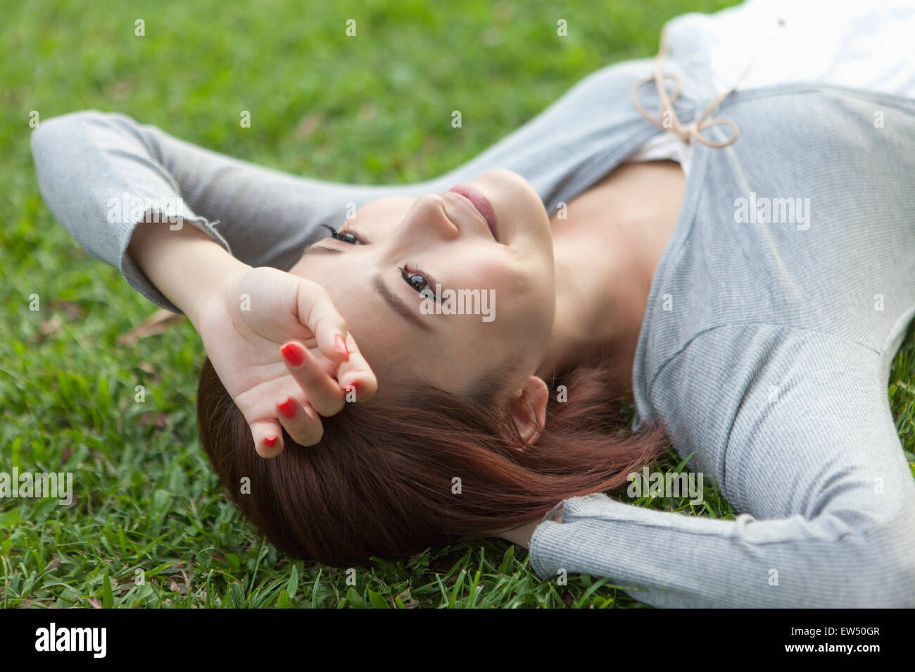 Giovane donna sdraiata sul prato con le mani sulla testa Foto Stock