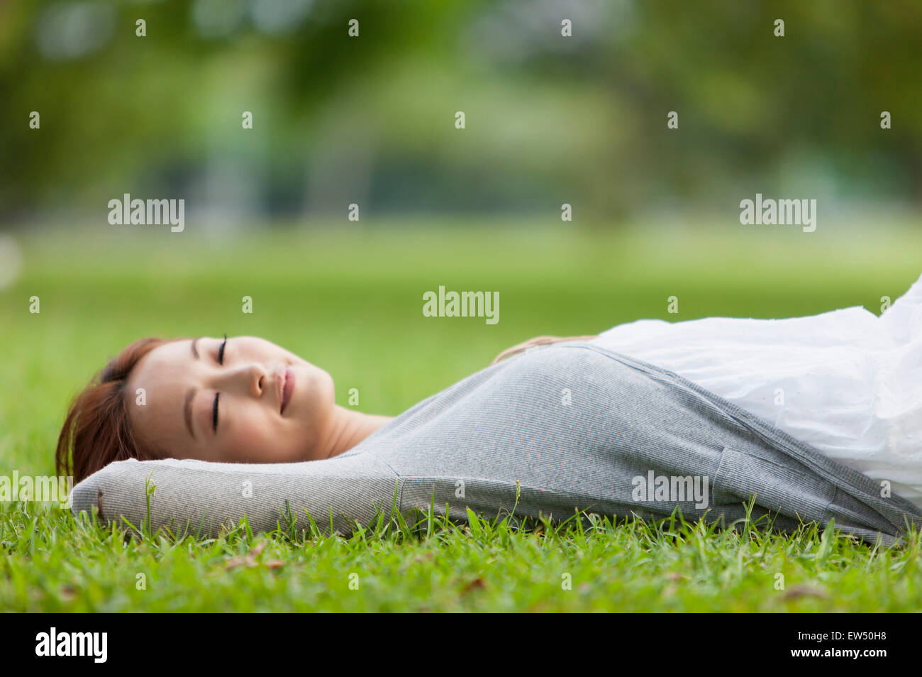 Giovane donna sdraiata sul prato con le mani sulla testa Foto Stock