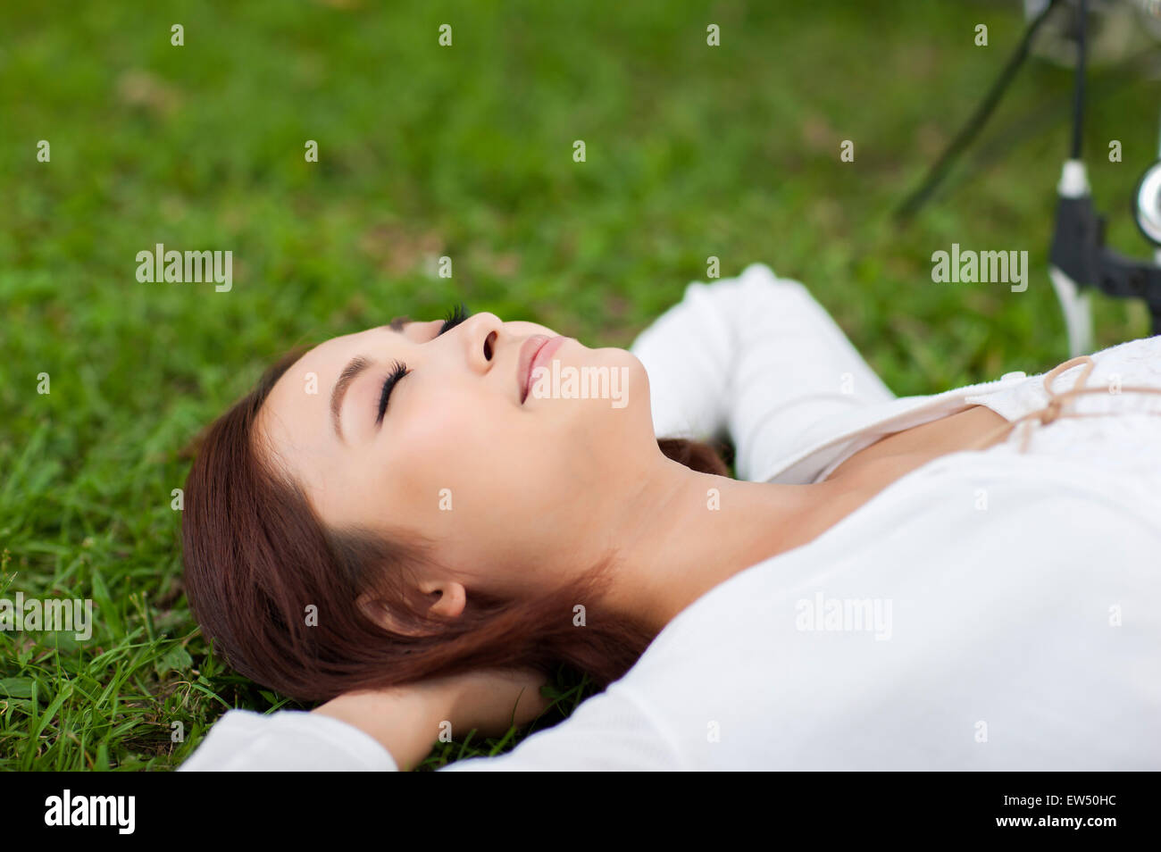 Giovane donna sdraiata sul prato con le mani dietro la testa Foto Stock