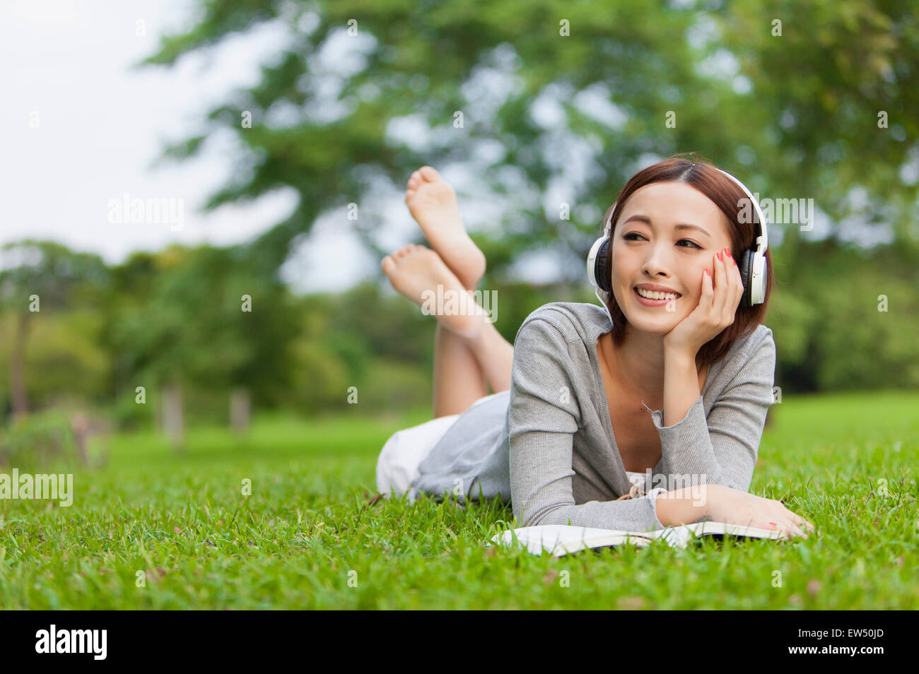 Giovane donna sdraiata sulla parte anteriore sul prato e guardando lontano con le cuffie Foto Stock