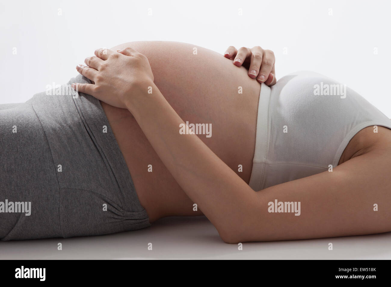 Donna incinta sdraiato con le mani sul ventre, Foto Stock