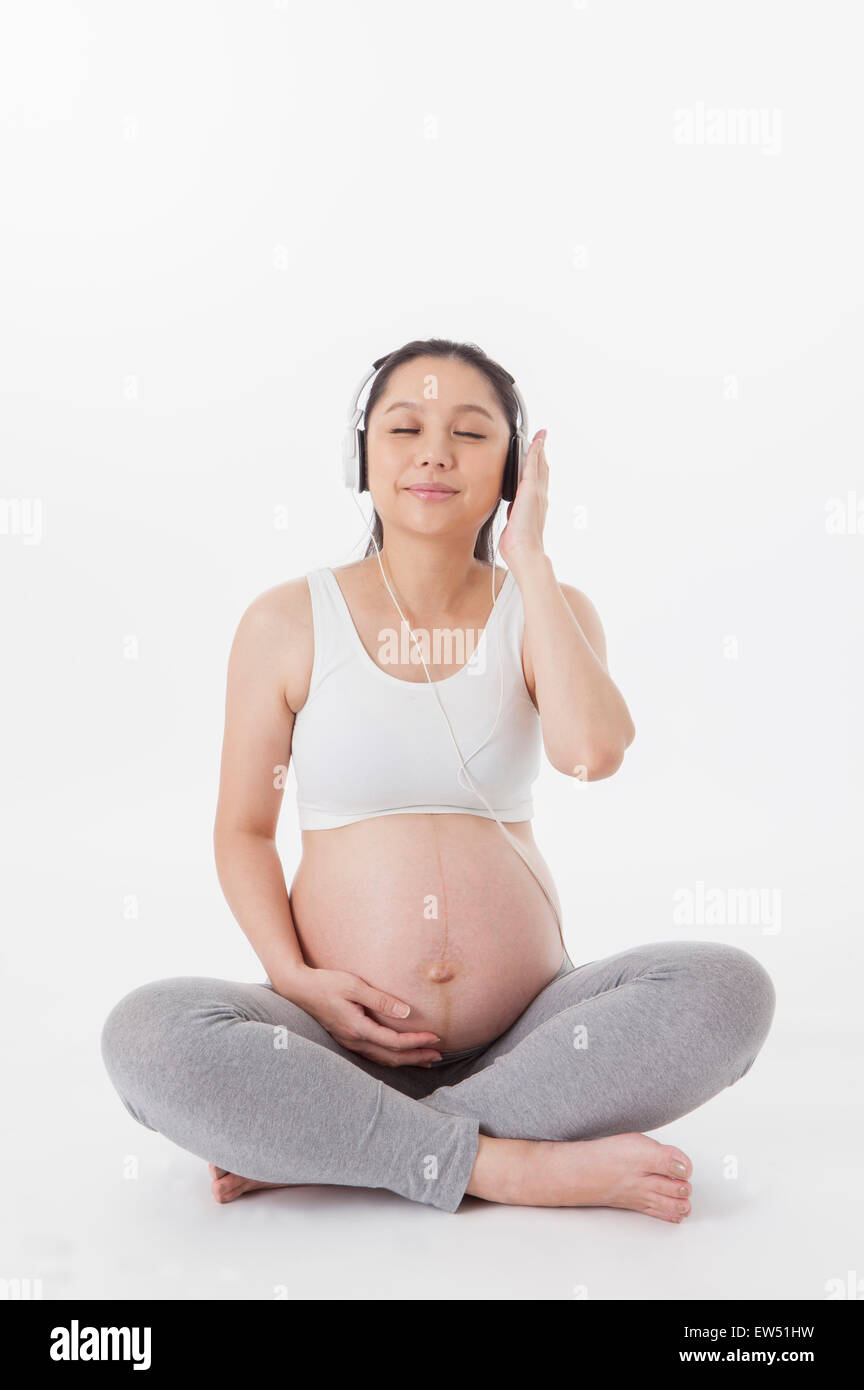 Donna incinta seduta sul pavimento e indossa le cuffie con gli occhi chiusi, Foto Stock