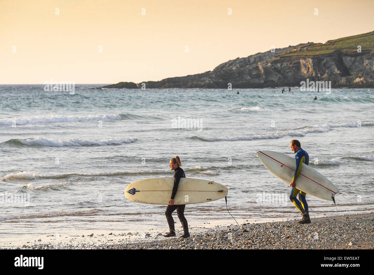 Due surfisti a piedi nel mare come il sole tramonta su Fistral Beach in Newquay, Cornwall. Regno Unito. Foto Stock