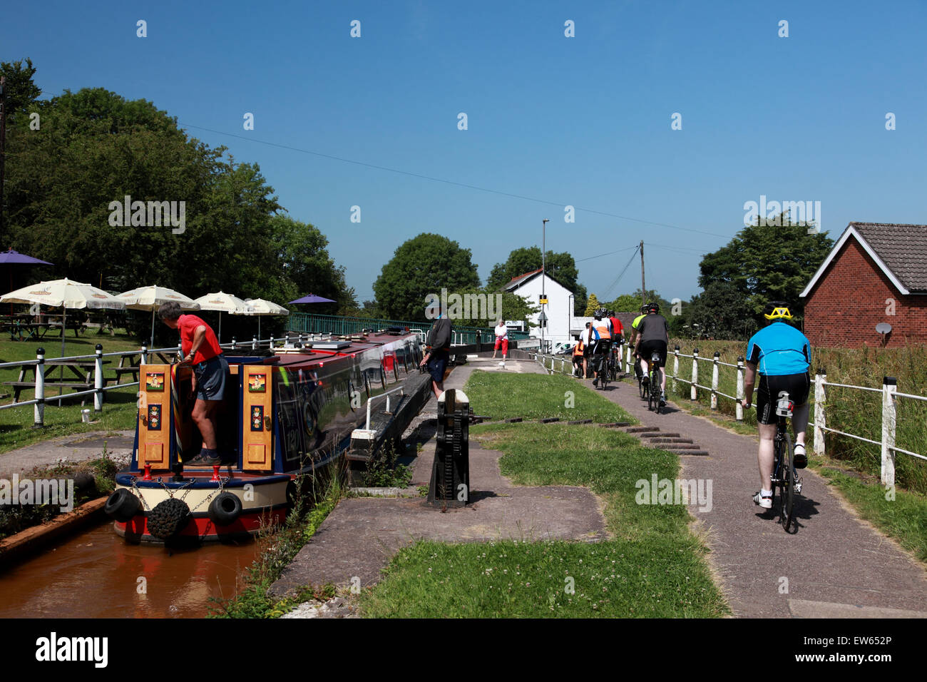 I ciclisti sul canal alzaia come narrowboat entra nella serratura 43 al Red Bull sul Trent & Mersey Canal a Kidsgrove, Staffordshire Foto Stock