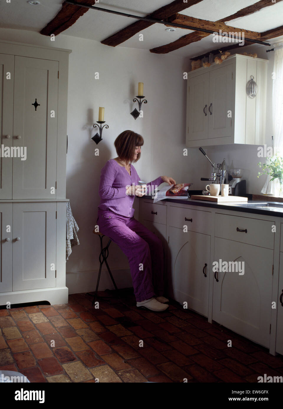 Donna seduta su uno sgabello e la lettura di un libro di cucina in un cottage cucina per solo uso editoriale Foto Stock