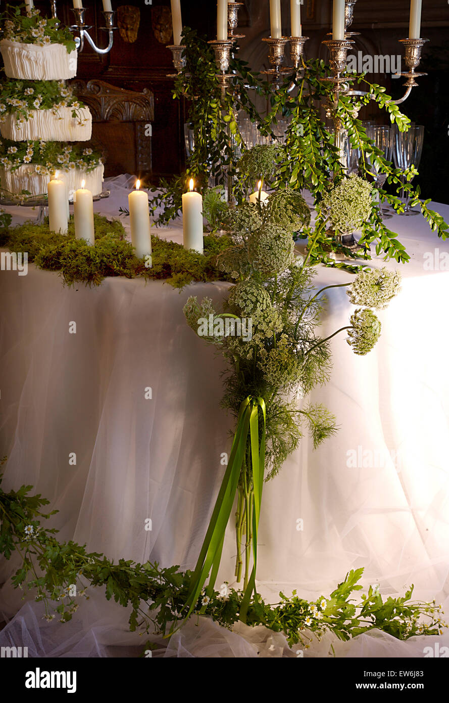 Candele e Ammi bianco fiori con fogliame e ghirlanda di fiori sul tavolo con set per un ricevimento di matrimonio Foto Stock