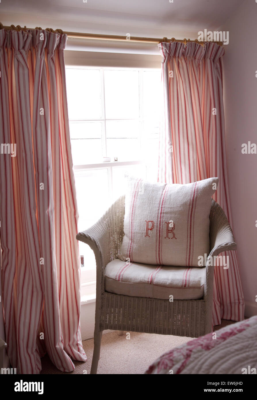 Monogrammed vintage cuscino di lino sul dipinto Lloyd Loom sedia davanti alla finestra con il rosa tende a strisce Foto Stock