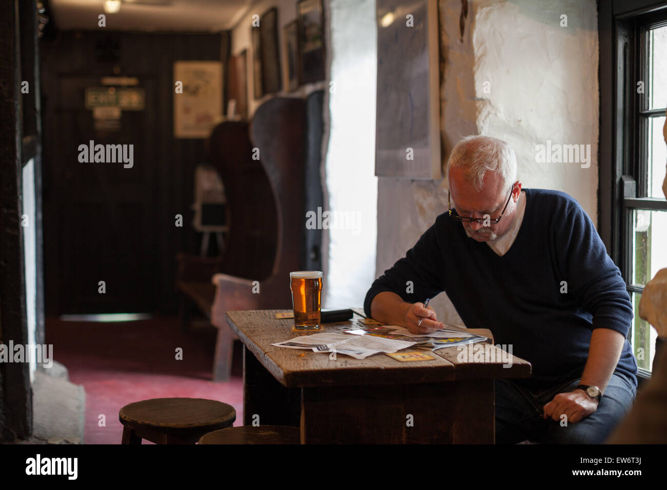 Un uomo si siede a un tavolo in un pub con una pinta di birra mentre la scrittura. Foto Stock