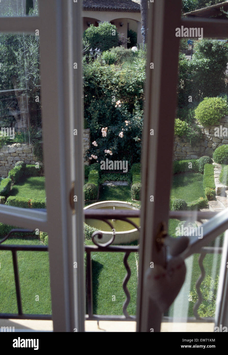 Vista attraverso le finestre francesi di un pendio terrazzato giardino con una piscina circolare nel sud della Francia Foto Stock