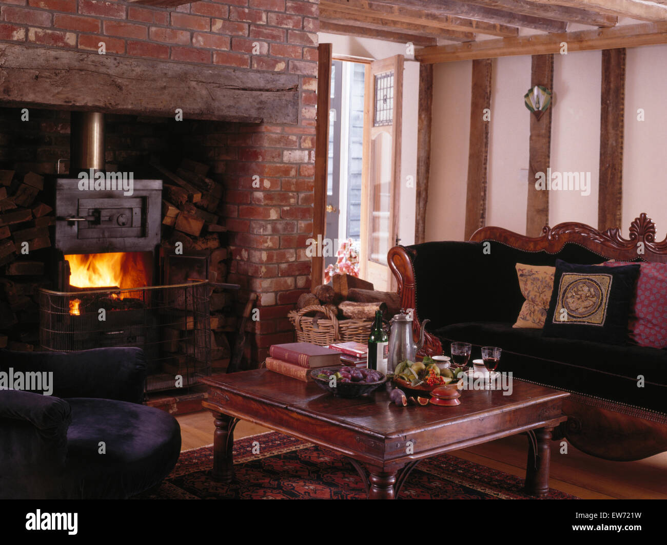 Stufa a legna nel camino inglenook in molto tradizionali cottage soggiorno con divano di antiquariato Foto Stock