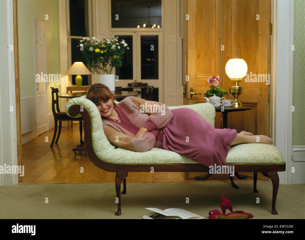 Giovane donna sdraiata su una chaise longue in uno degli anni settanta soggiorno Foto Stock
