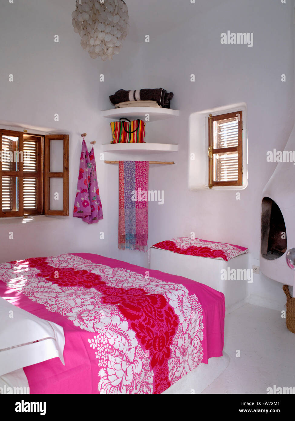Rosa luminoso bed-coperchio sul letto in bianco camera da letto marocchino con angolo semplici ripiani e persiane in Windows Foto Stock