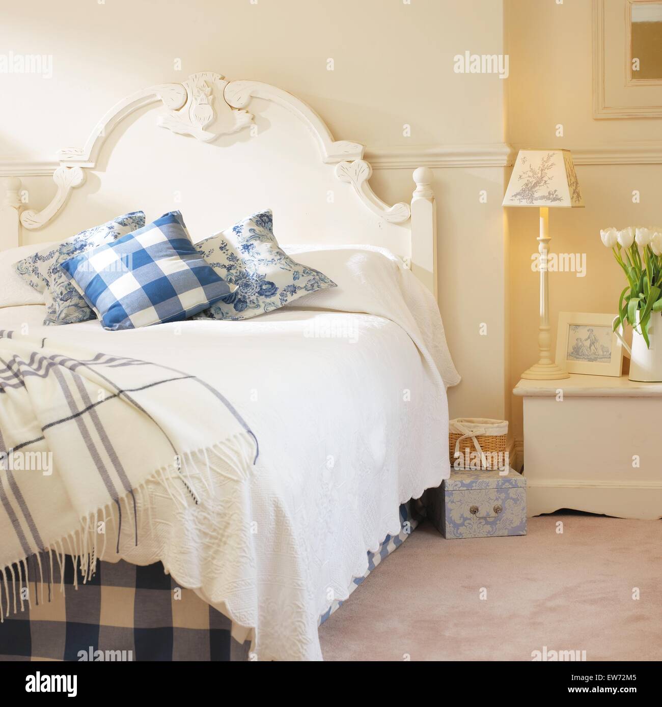 Blue+bianco a scacchi buttare e cuscini sul dipinto di bianco letto con trapunta bianca in camera da letto bianca con la lampada accesa sul comodino Foto Stock