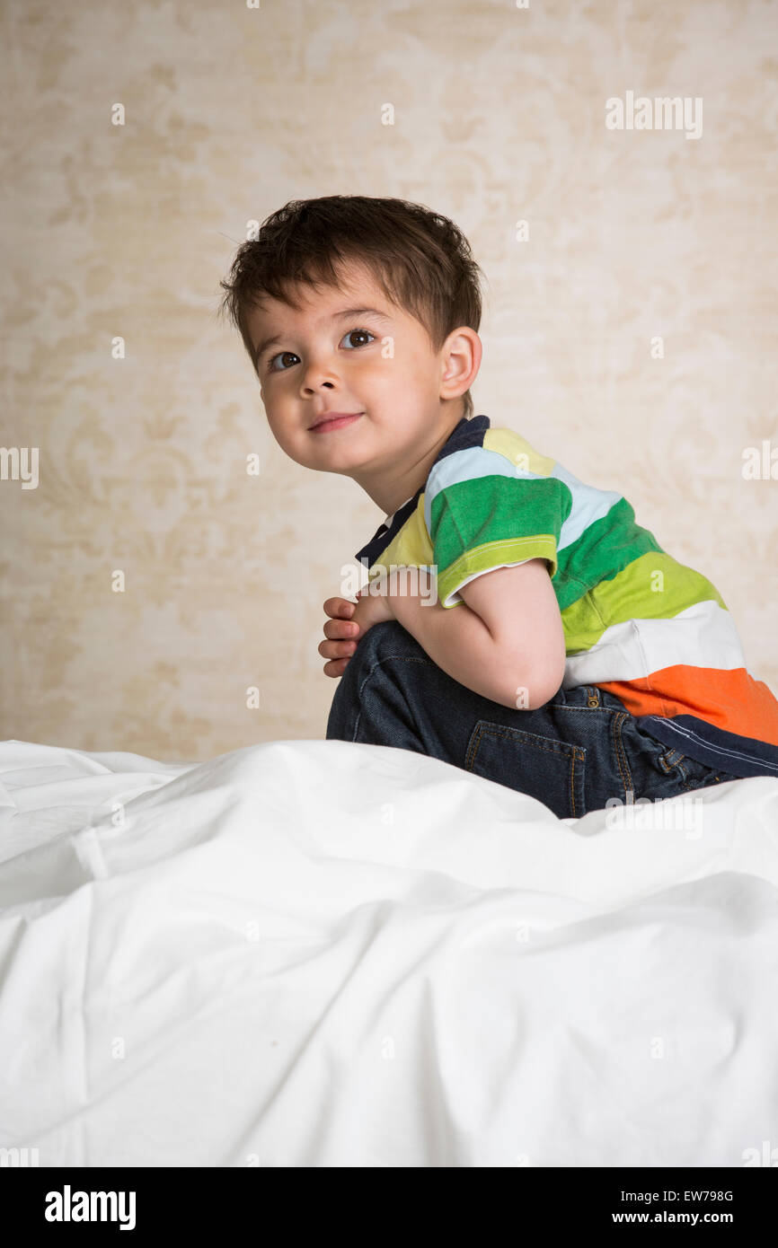 Piccolo Ragazzo seduto su un letto Foto Stock