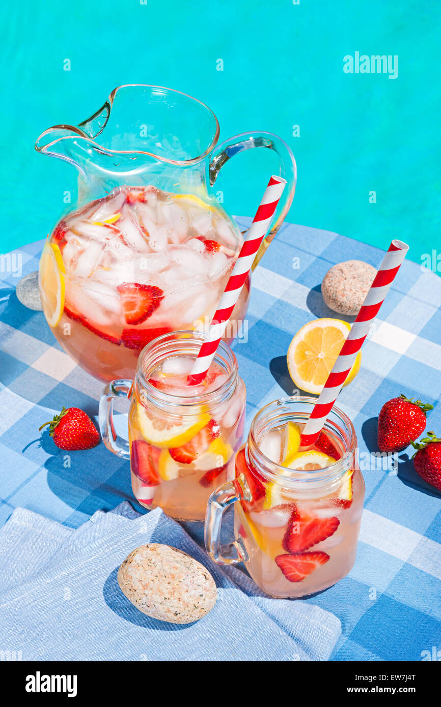 Di ghiaccio freddo in casa fragola limonata in caraffa e bicchieri di carta con cannucce in estate outdoor pool side table Foto Stock