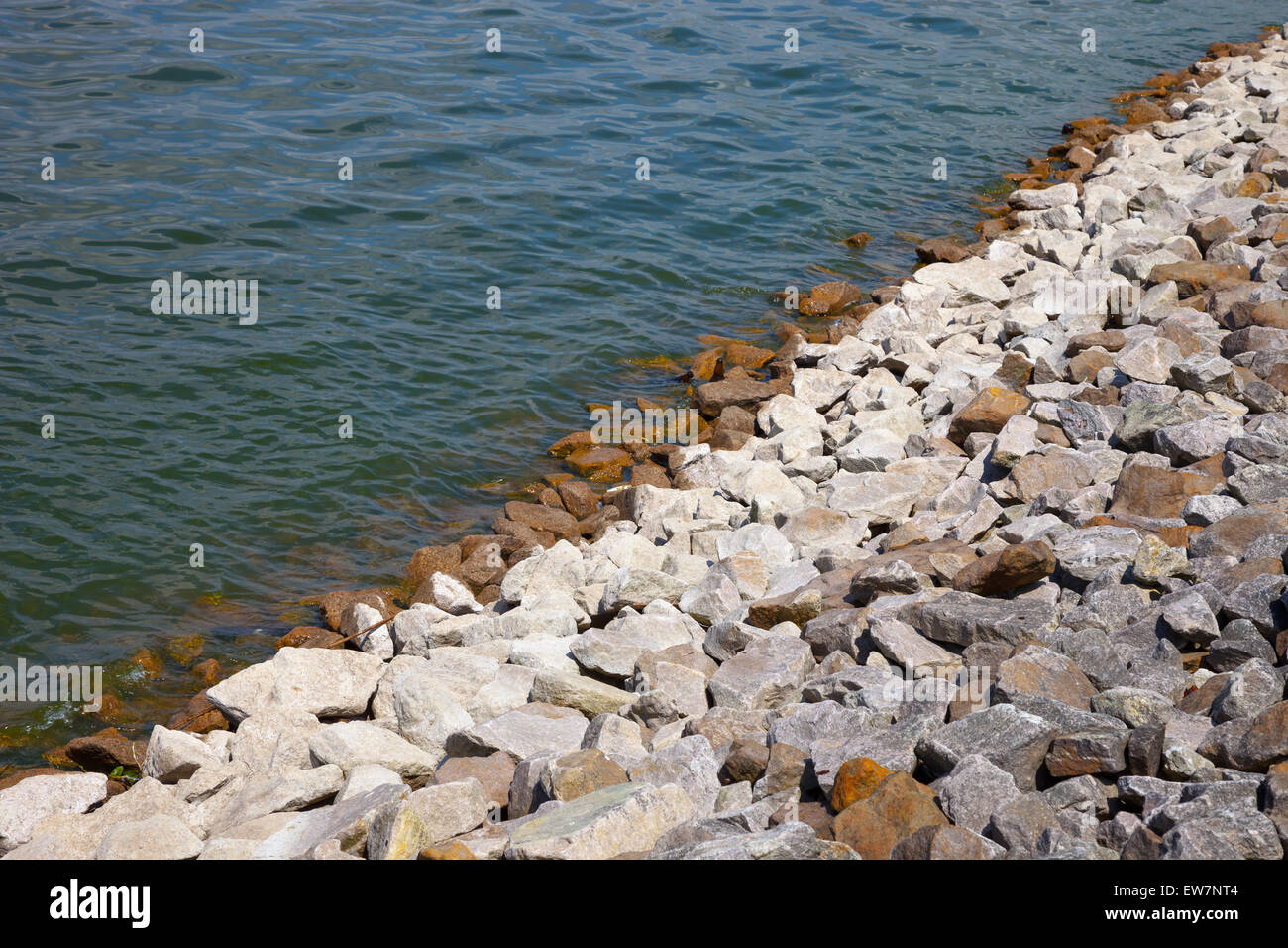 Banca di pietra del lago artificiale con grandi pietre naturali e acque torbide. Foto Stock