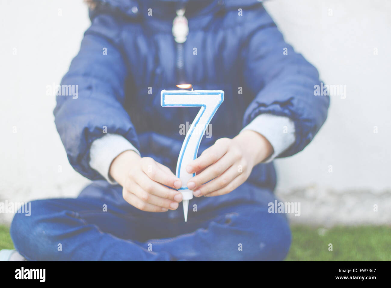Ragazza seduta zampe trasversale tenendo un numero sette candela Foto Stock