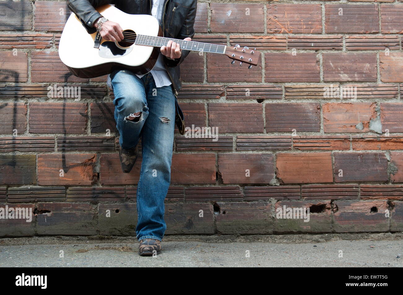 Uomo in giacca di pelle e stivali da cowboy di suonare la chitarra in un vicolo Foto Stock