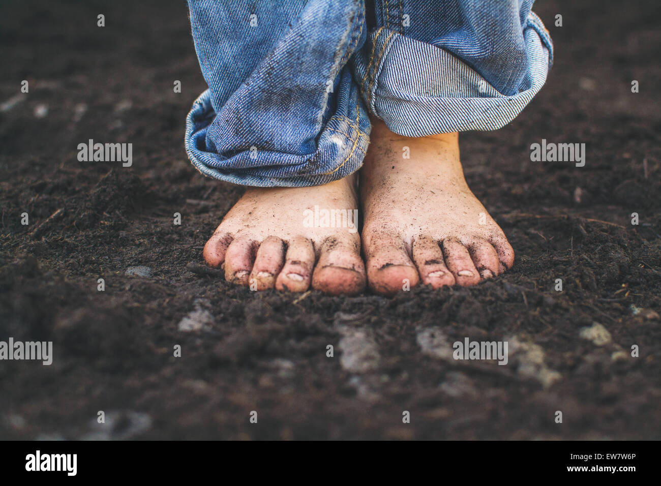 Primo piano dei piedi sporchi di un ragazzo che si trova nel terreno Foto Stock